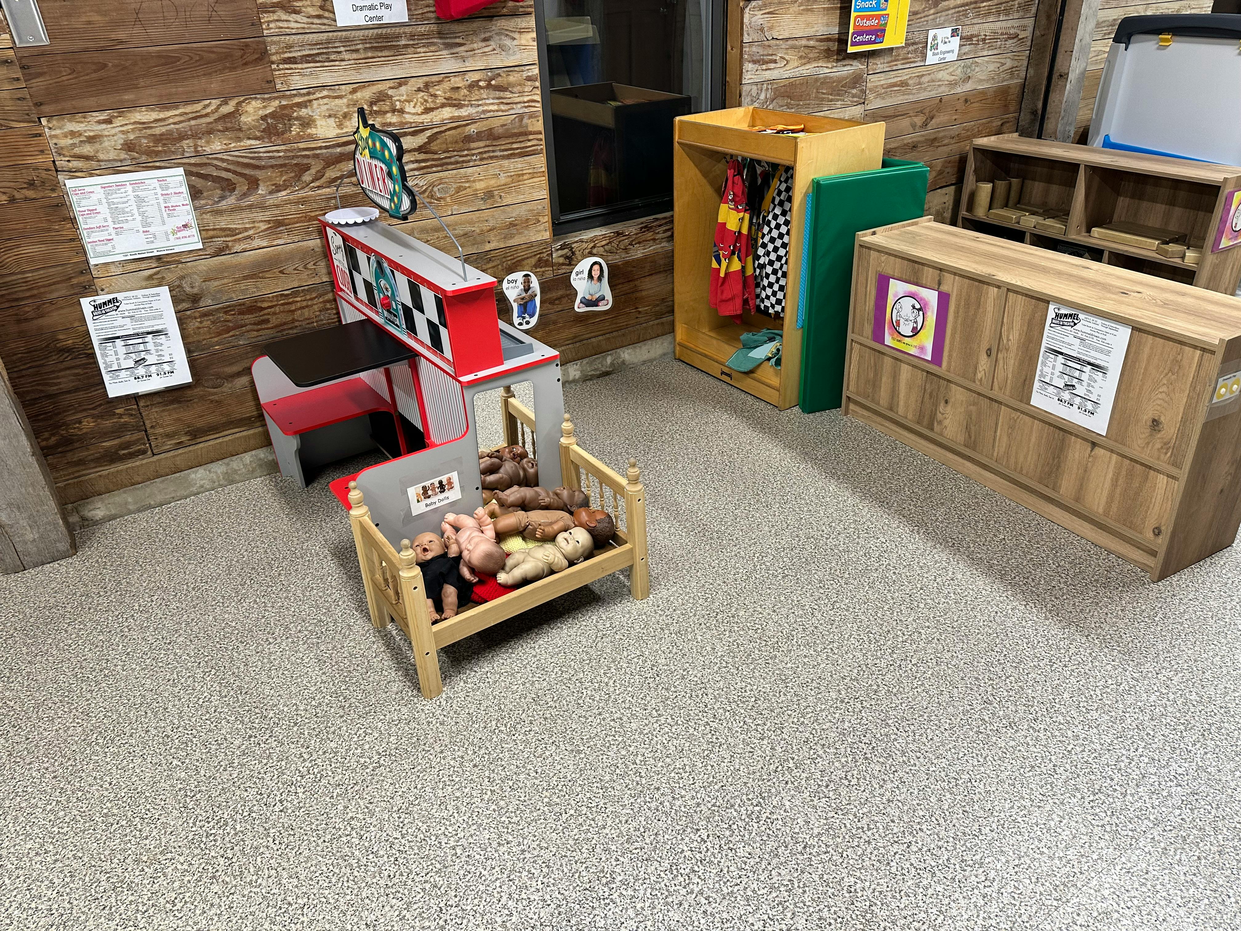 Dolls in a crib next to a toy house in a classroom