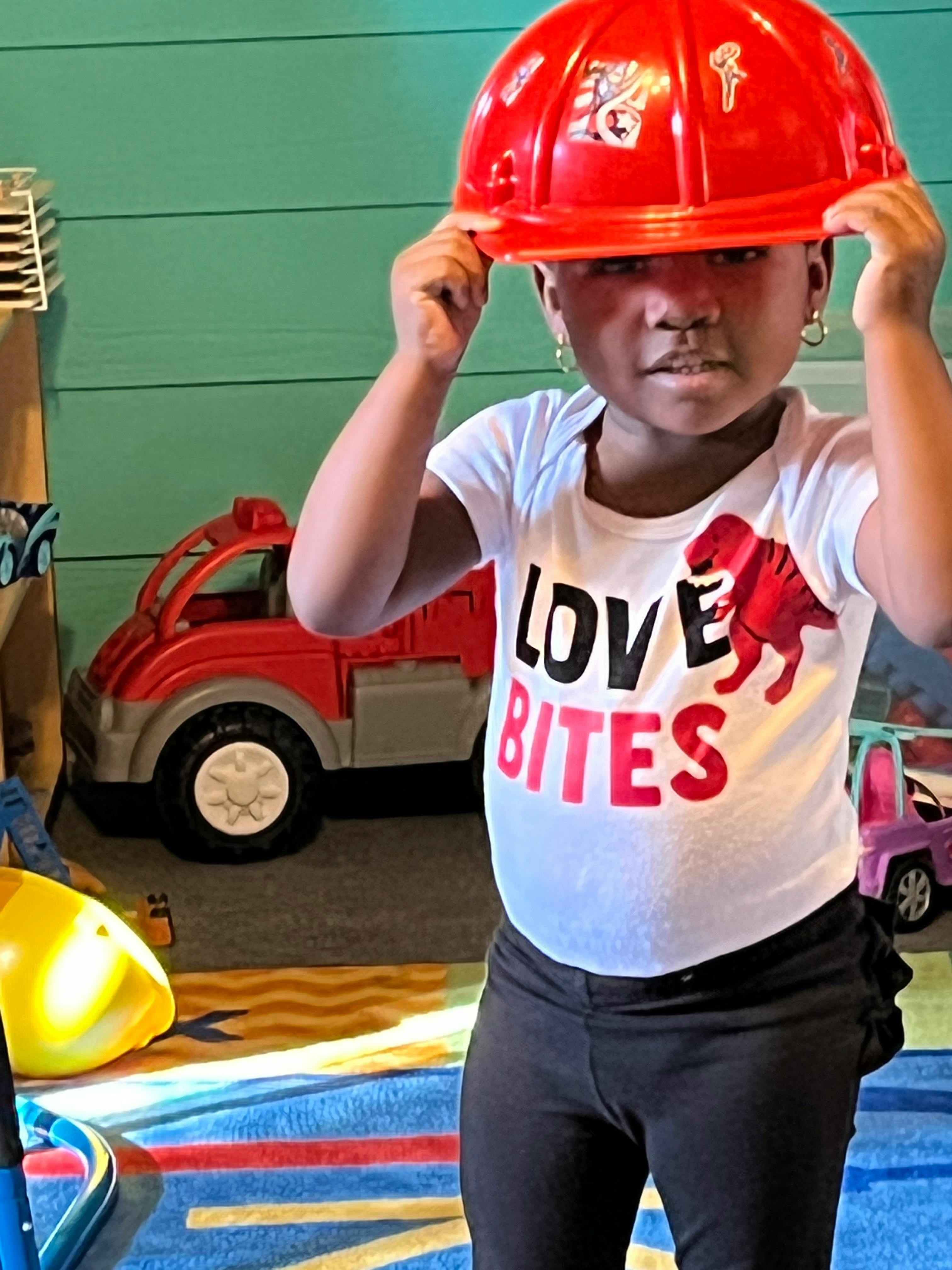 Child wearing a red hard hat and a shirt that says "Love Bites"