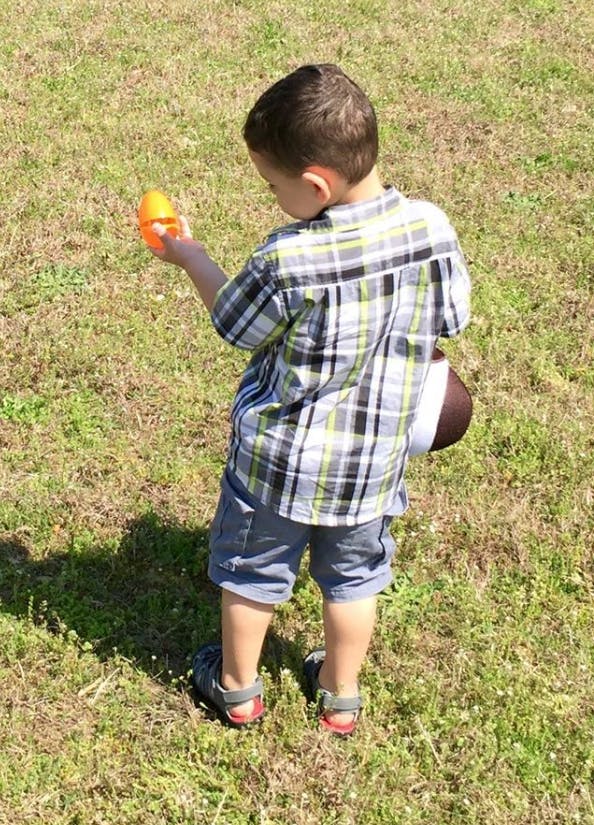 Child holding an orange plastic egg and a football on grass