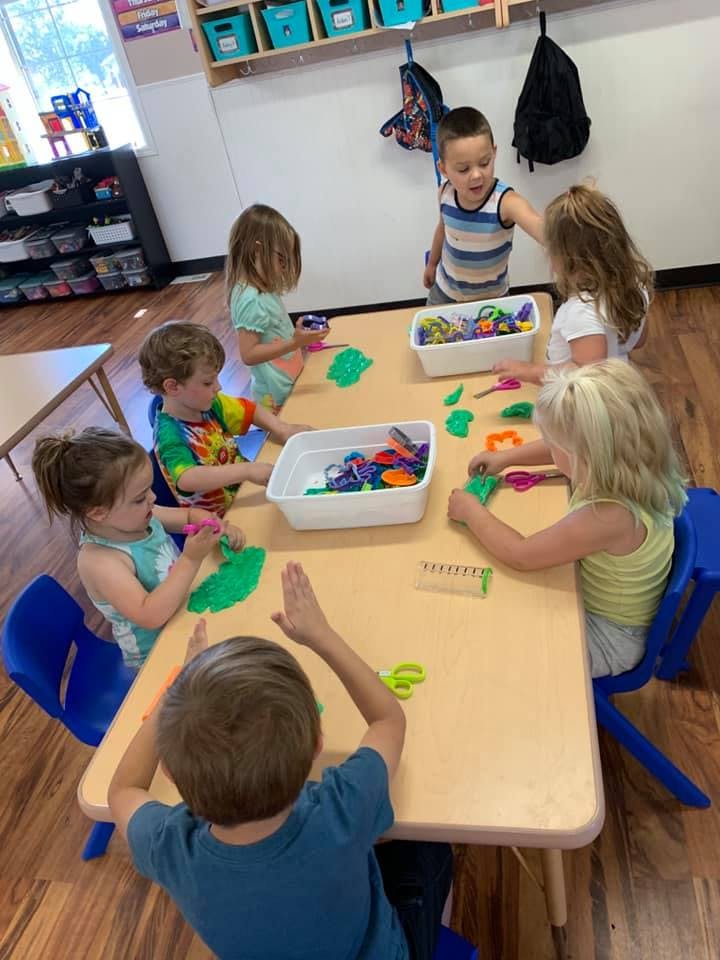 Children playing with modeling clay and tools at a table in a classroom