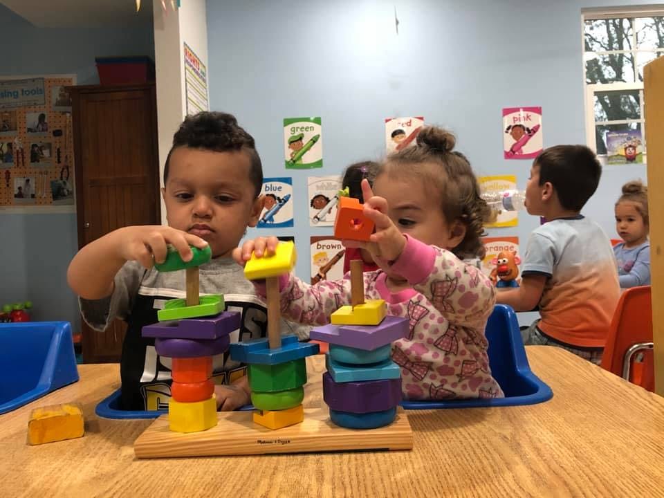 Two children playing with stacking toys at a table in a classroom