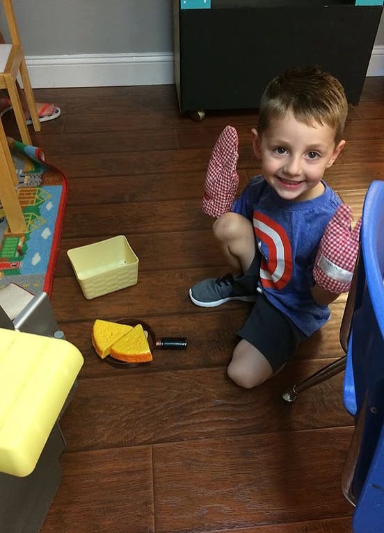 Child kneeling on floor wearing oven mitts with toy food