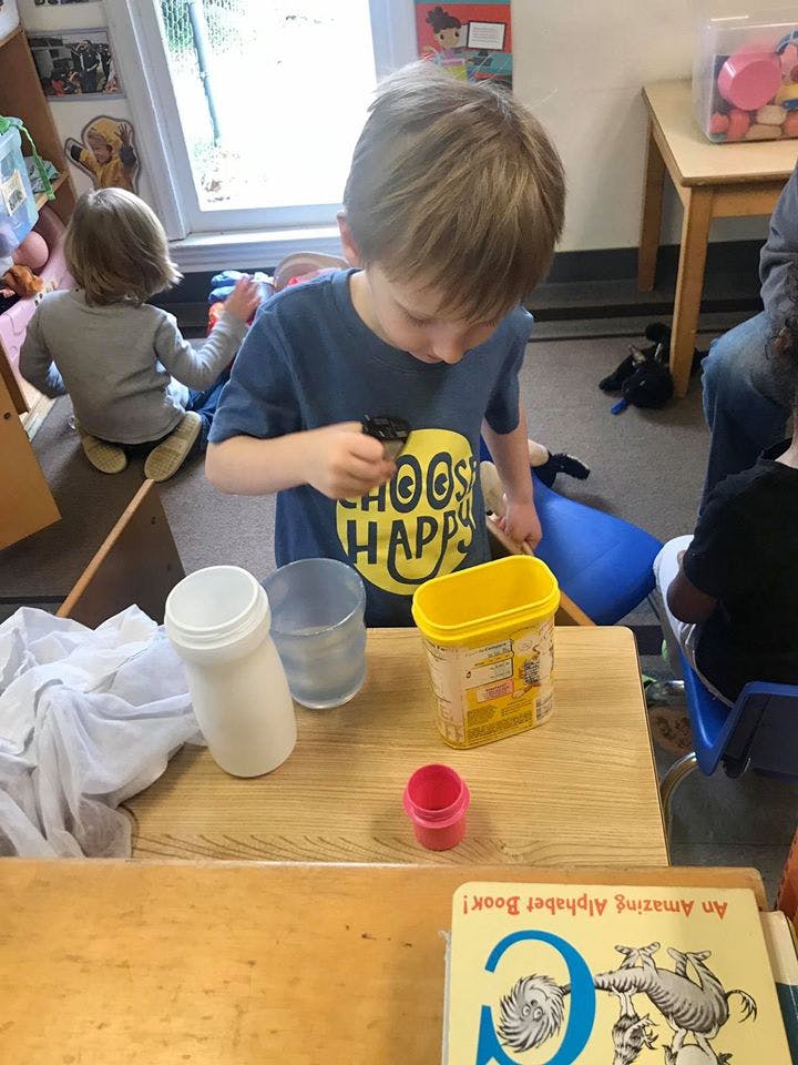 Child in a blue shirt holding a small object over containers on a table