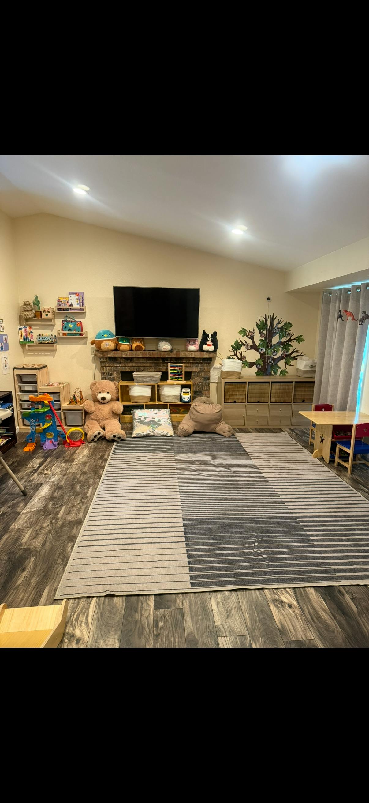 Playroom with toys, storage units, a large rug, and a television over fireplace