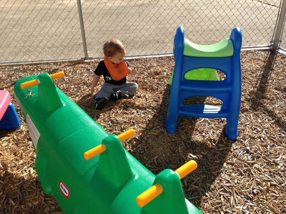 Child sitting on wood chips next to playground equipment