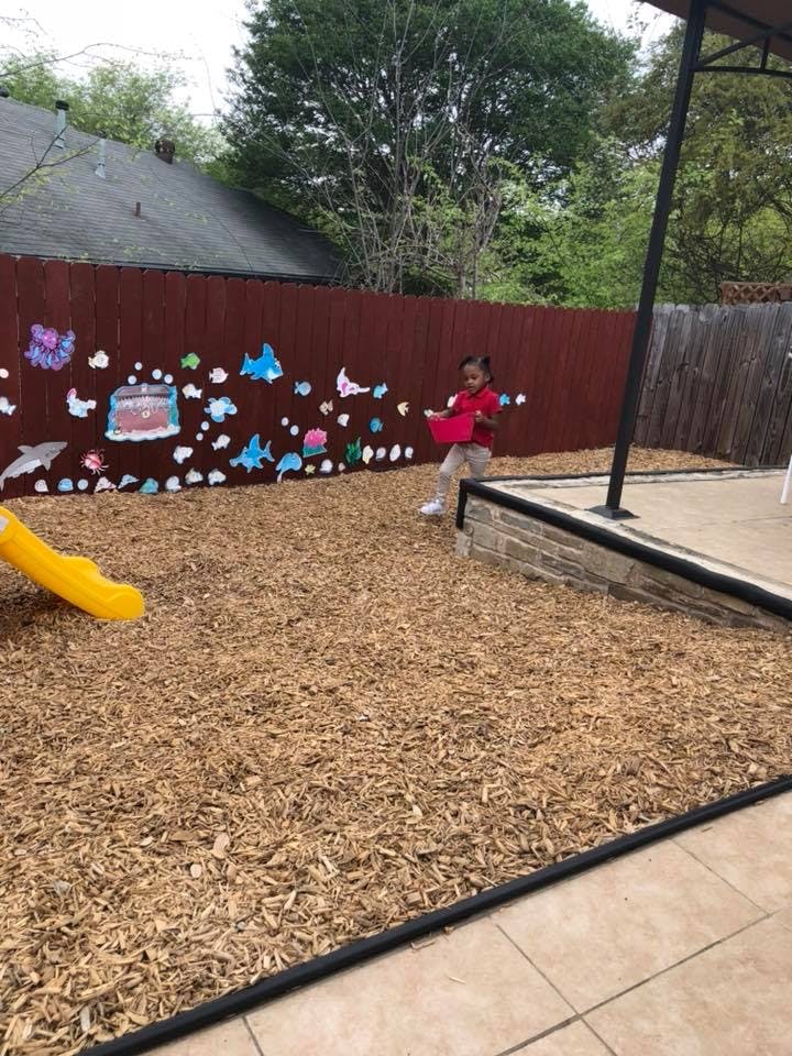 Child in a red shirt holding a red bucket in a wood chip play area