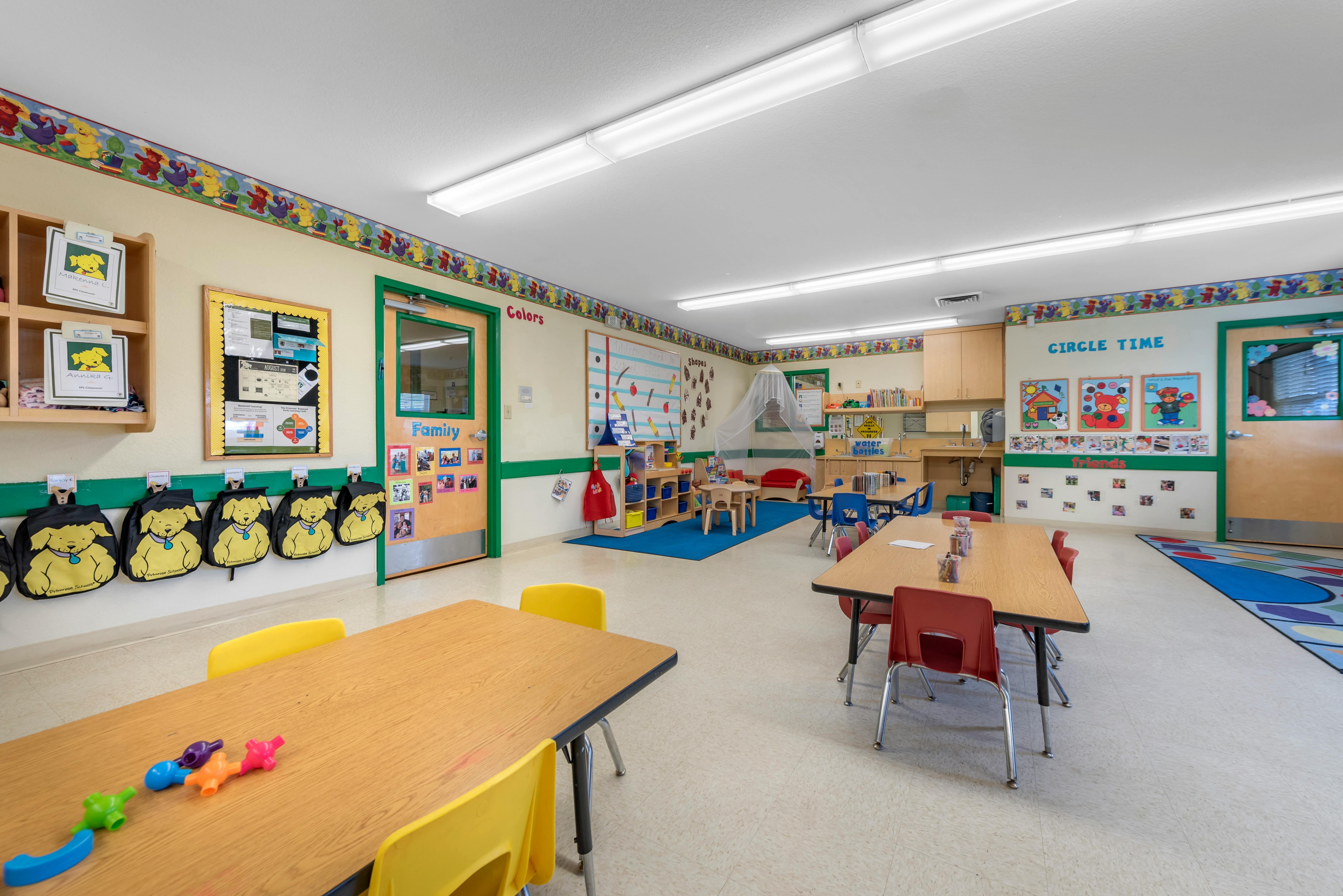 Empty classroom with tables and chairs, artwork on walls, and colorful decor