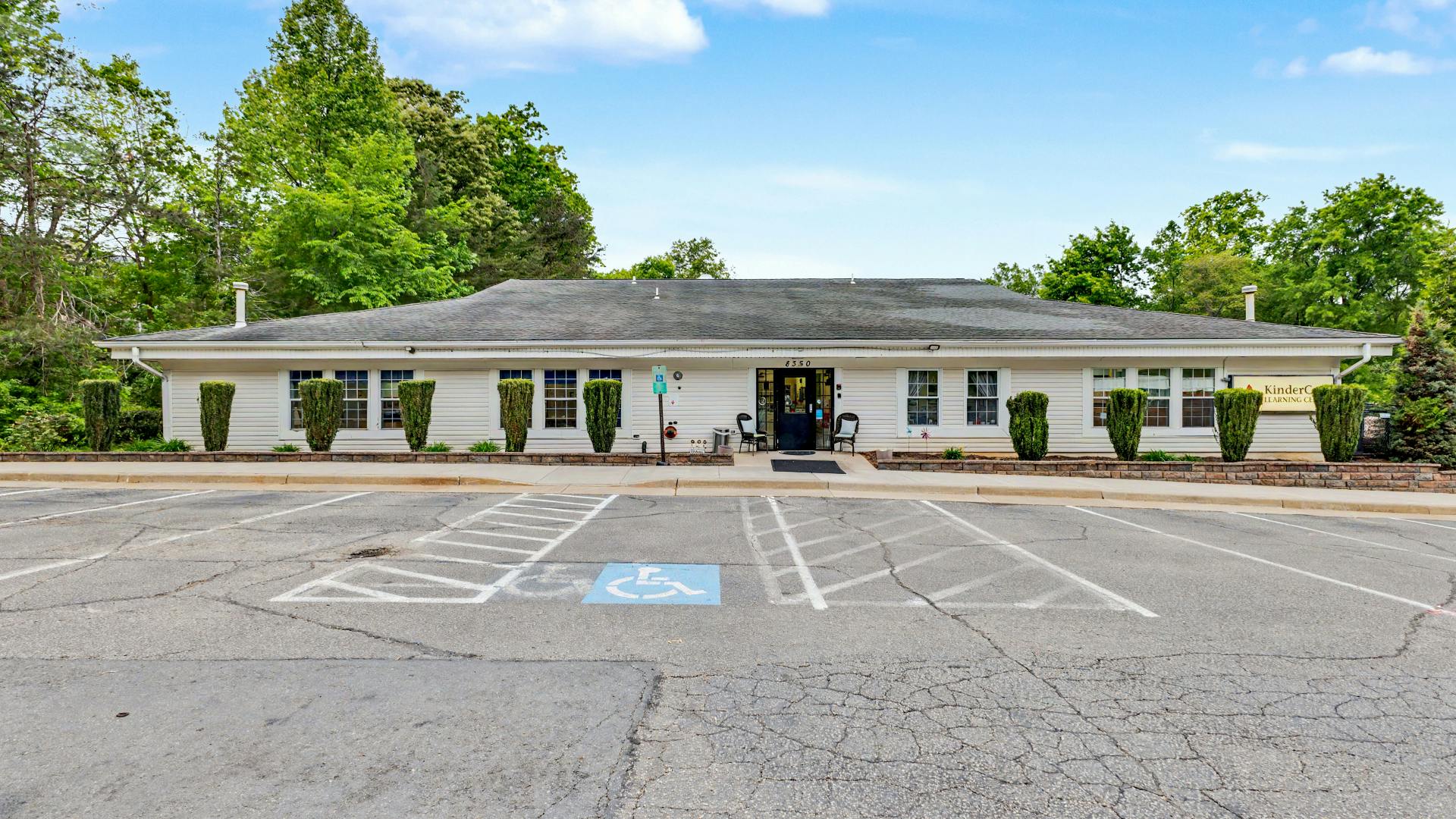 White building with a parking lot in front and green trees in the background