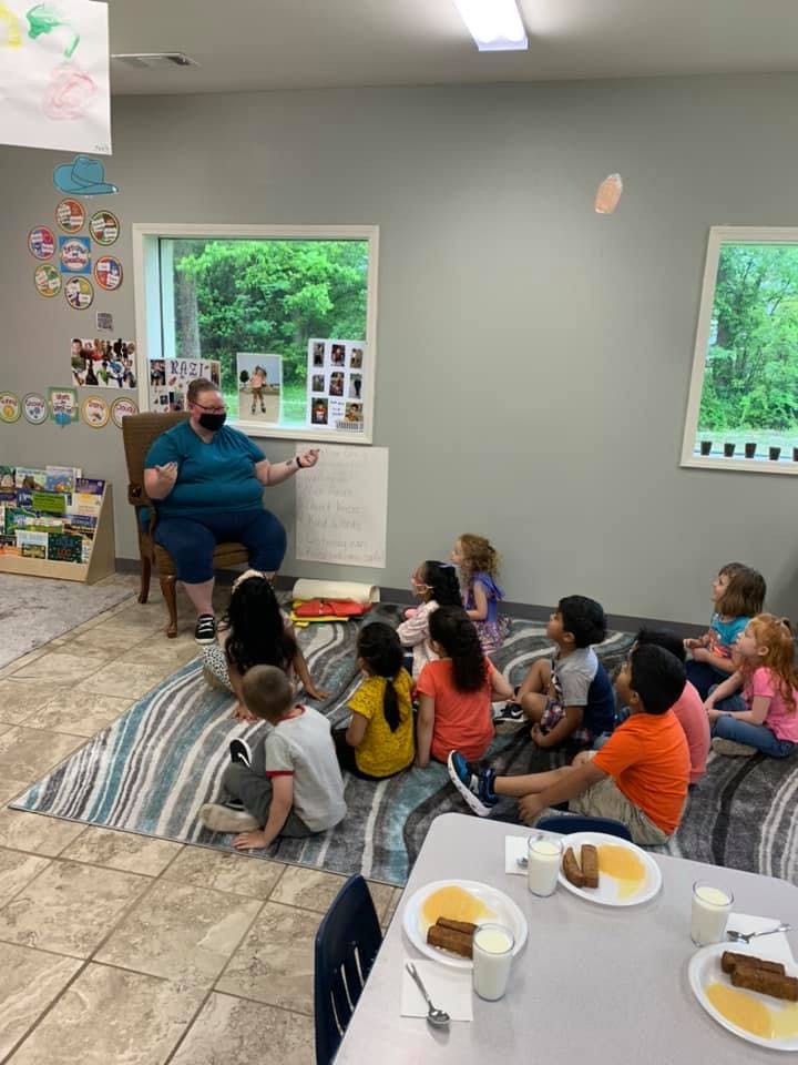 Person in a mask sitting in a chair with children sitting on the floor