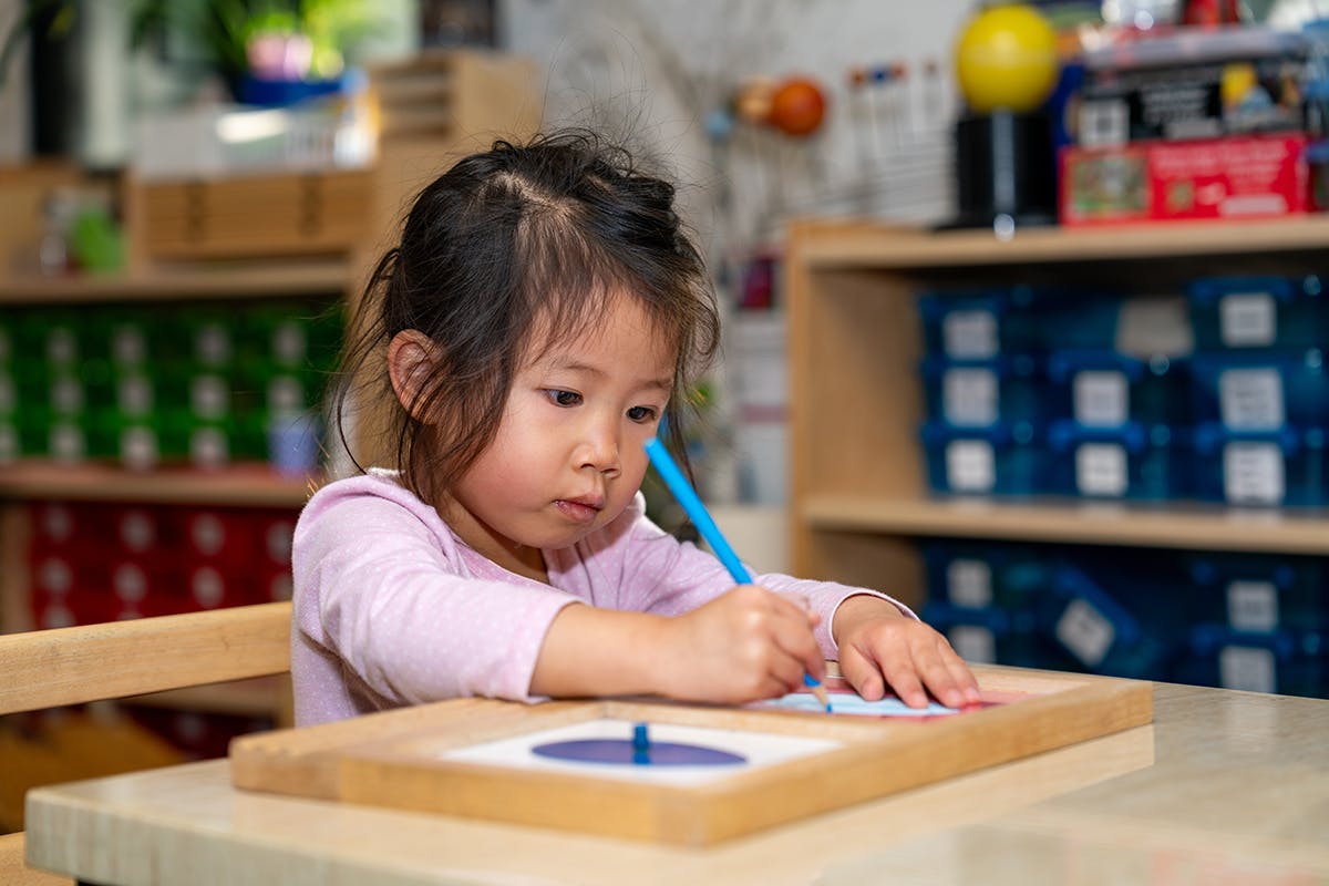 Child drawing with a blue pencil at a table in a classroom
