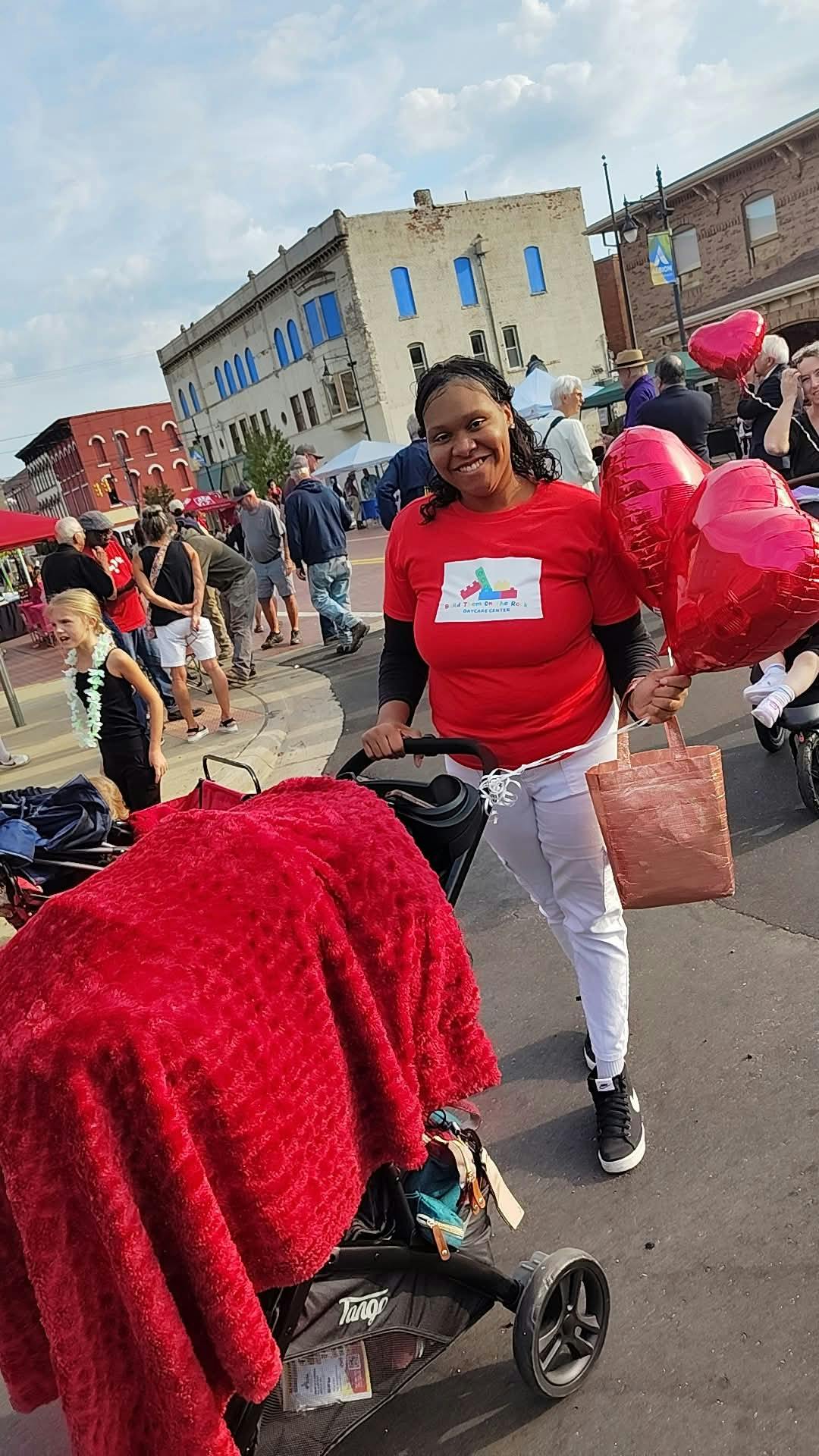 Person pushing a stroller and holding heart-shaped balloons