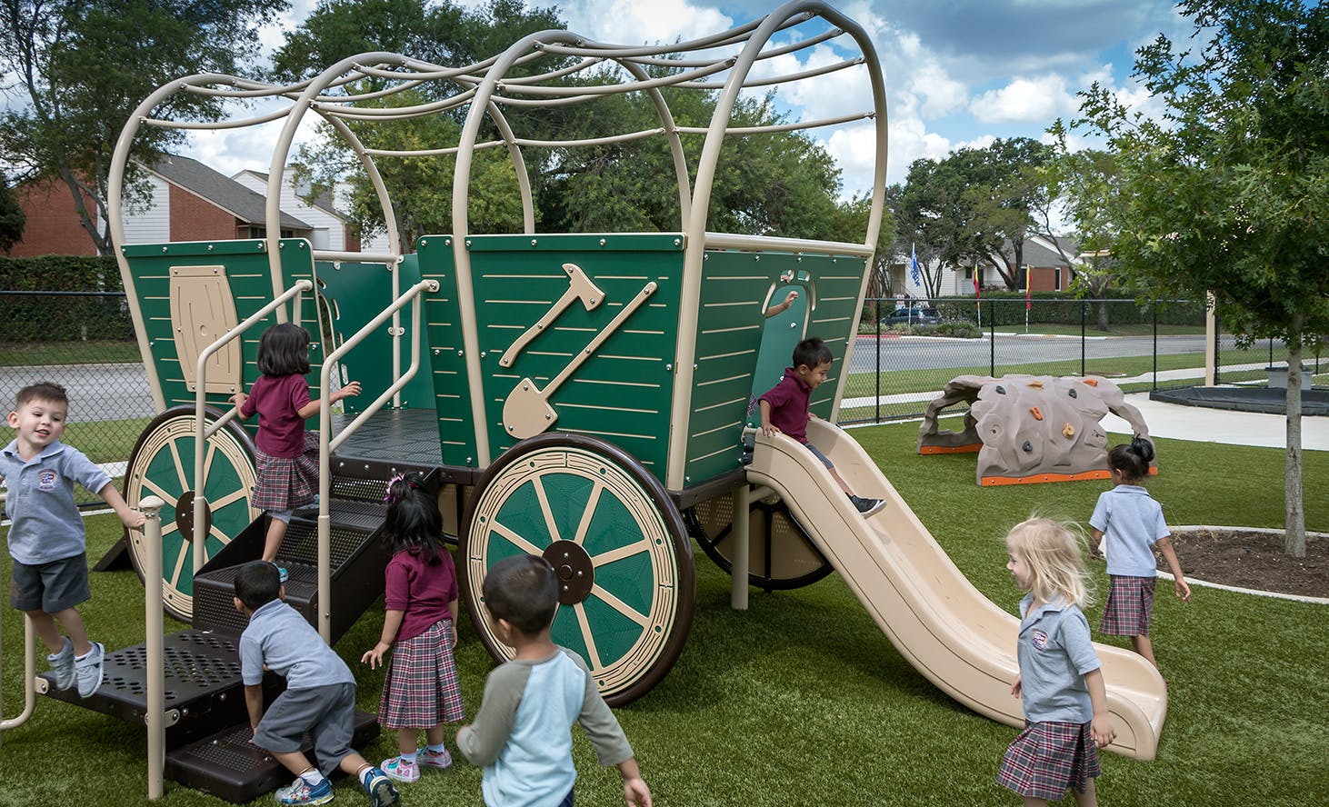 Children playing on a wagon-shaped playground structure with a slide