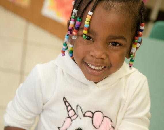 Child with beaded braids wearing a white unicorn hoodie