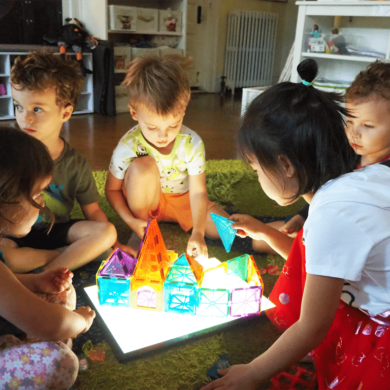 Children playing with colorful magnetic tiles on a light board