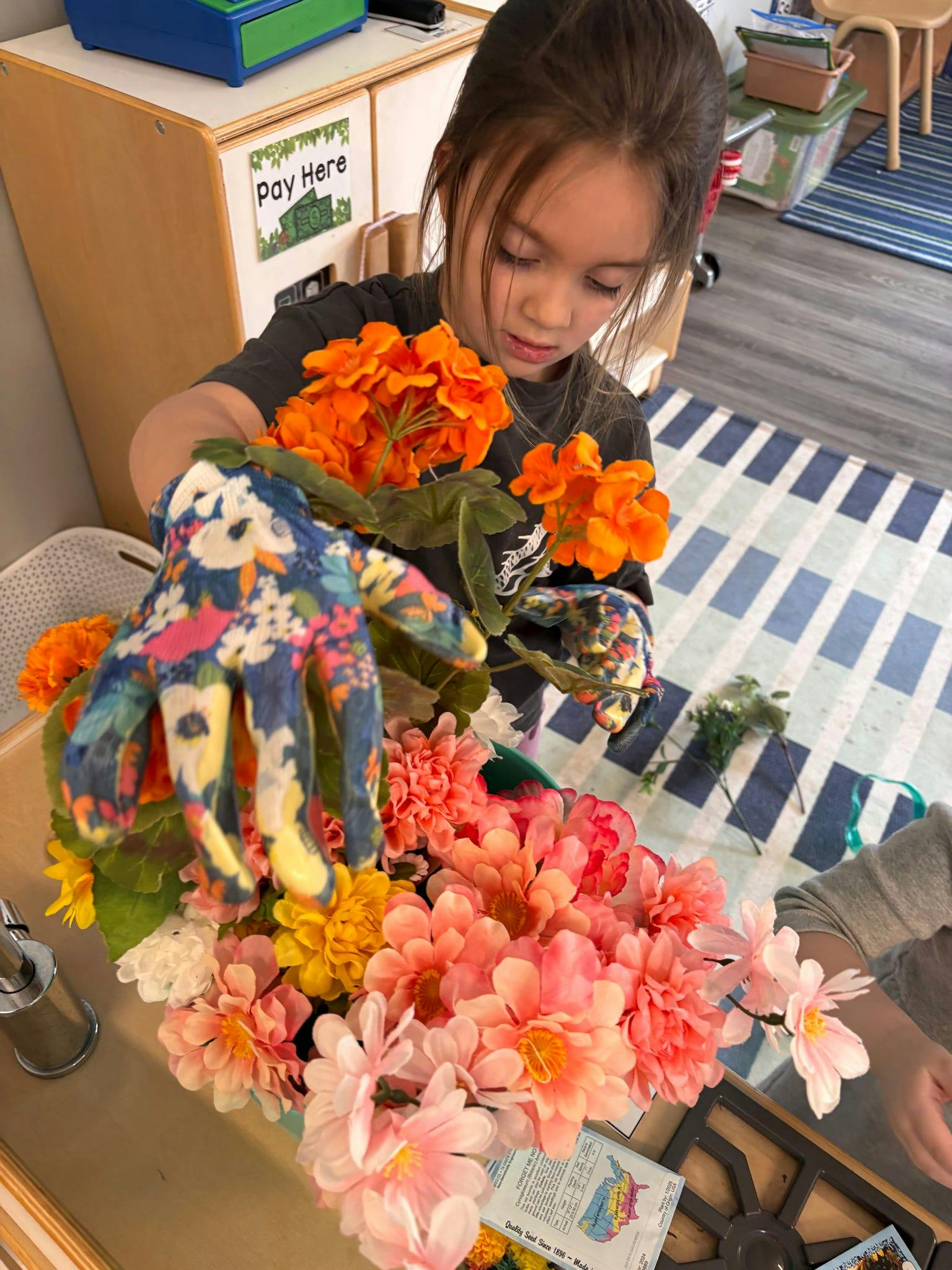 Child wearing floral gloves arranging artificial flowers in a classroom