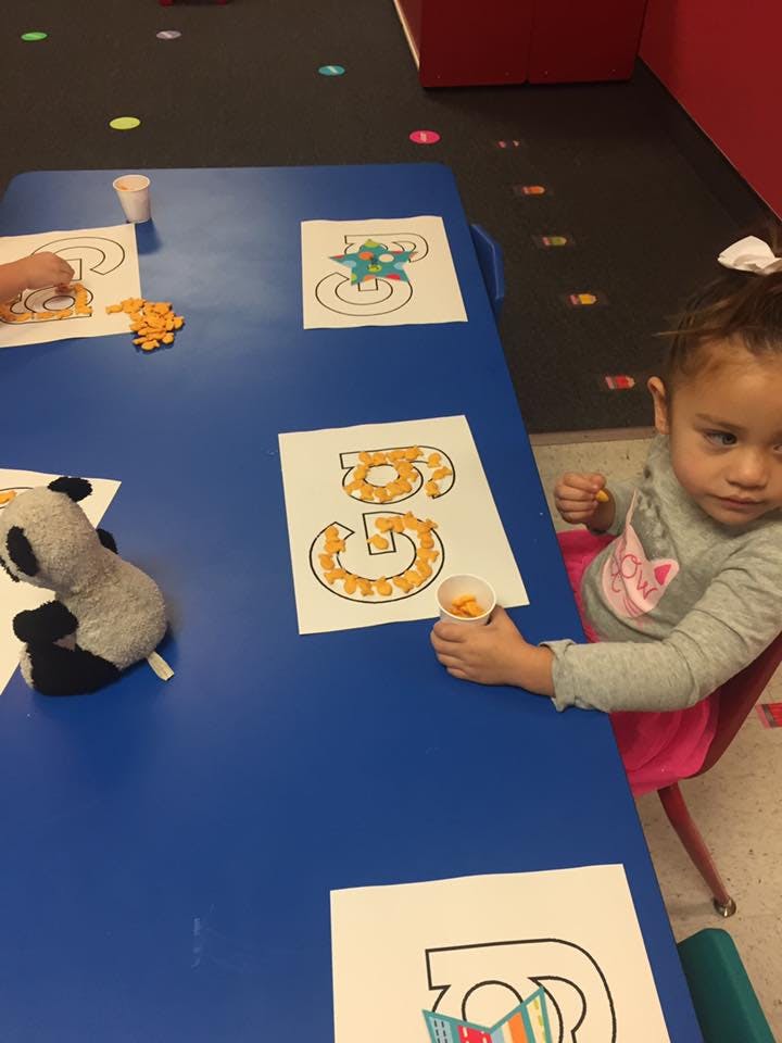 Child at a table with number outlines filled with small snacks