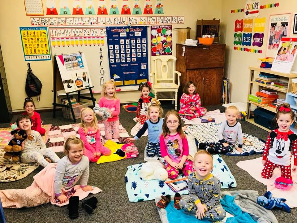 Group of children in pajamas sitting on blankets in a classroom