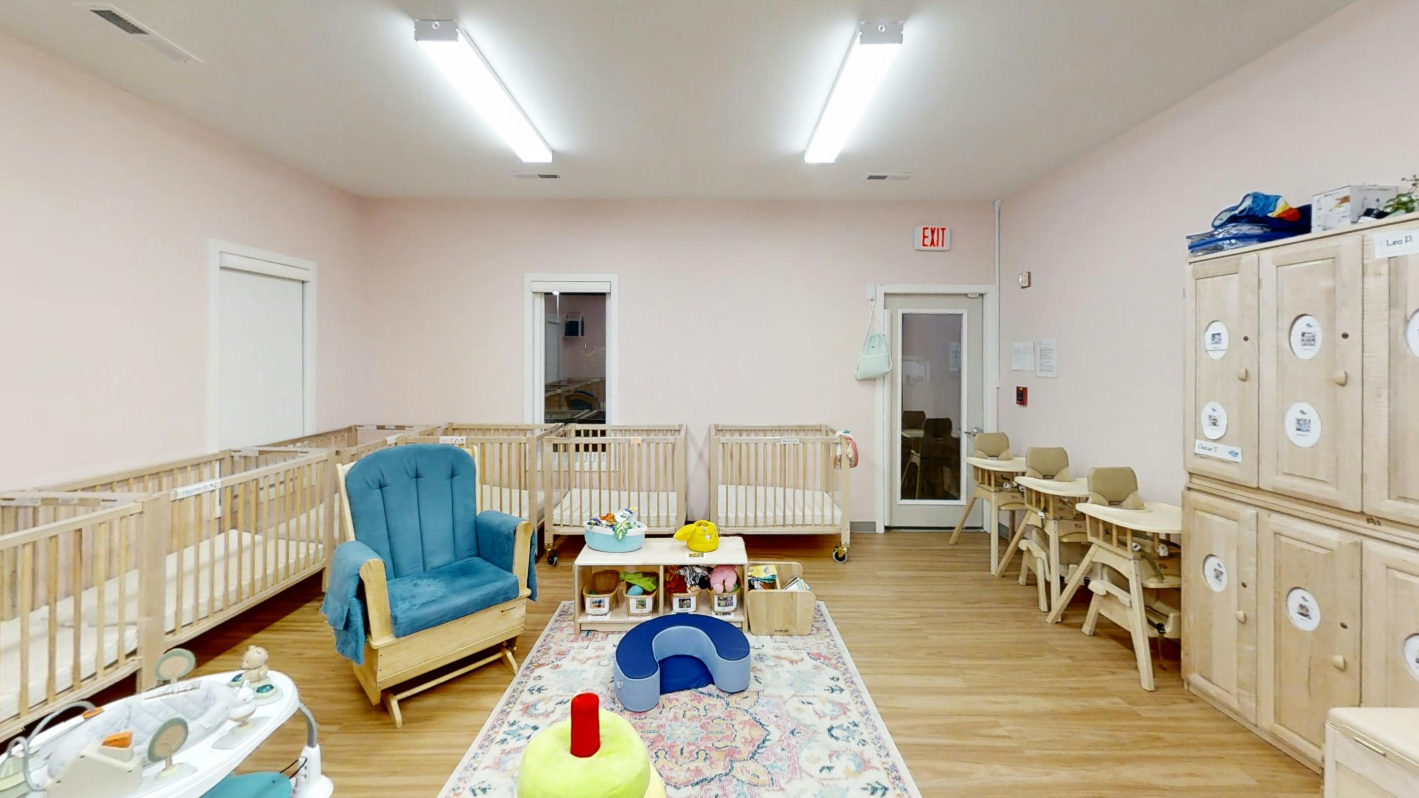 Nursery room with multiple cribs, a blue armchair, and small tables