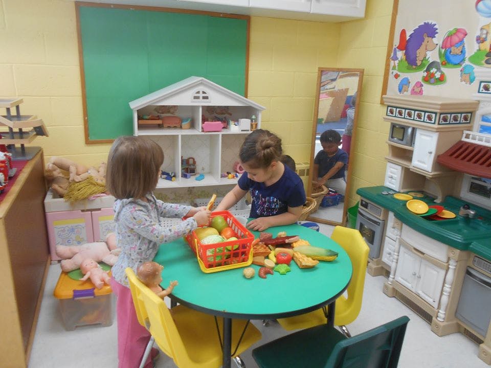 Two children playing with toy food at a table in a classroom