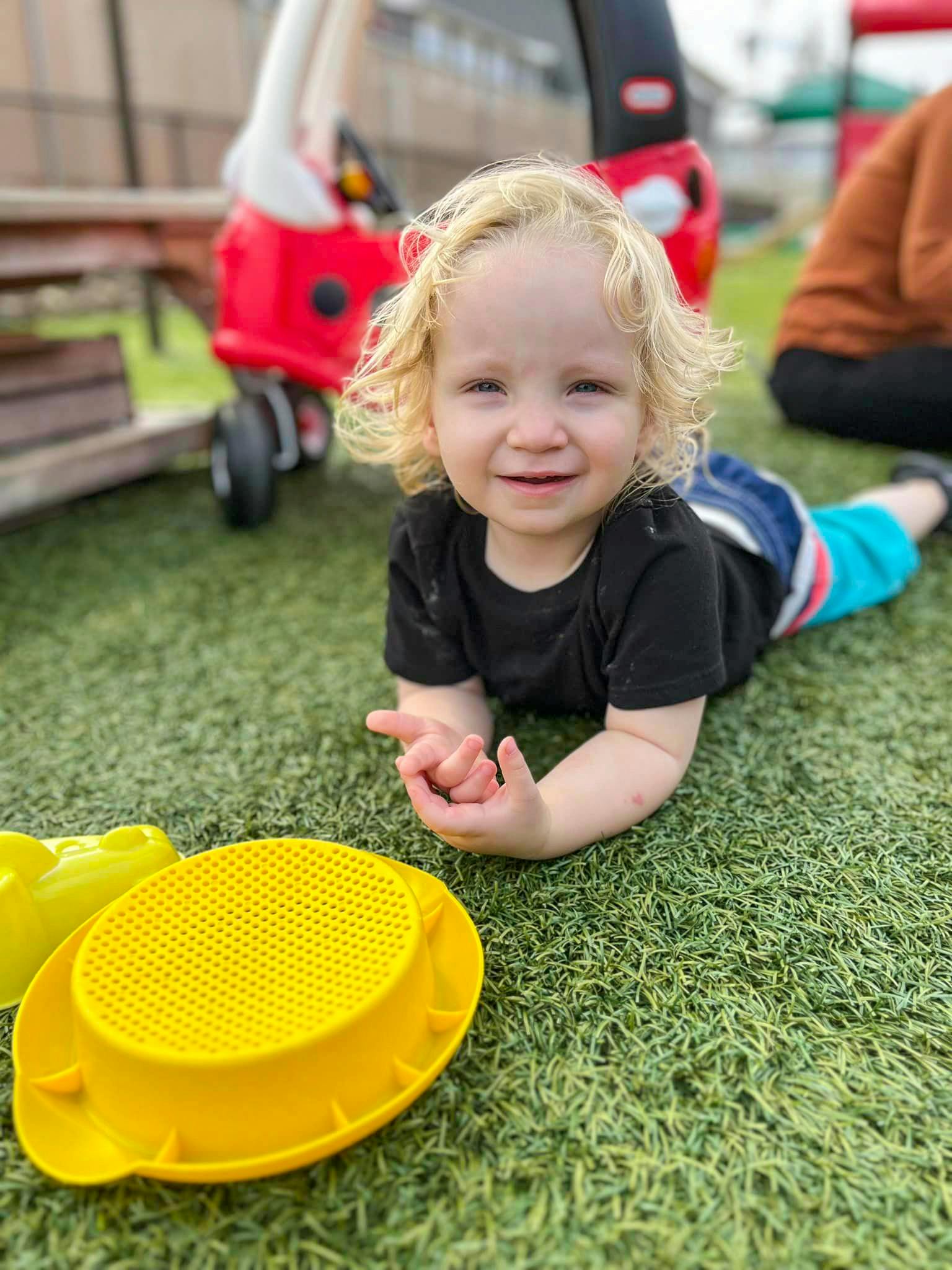 Child lying on artificial grass with a yellow toy