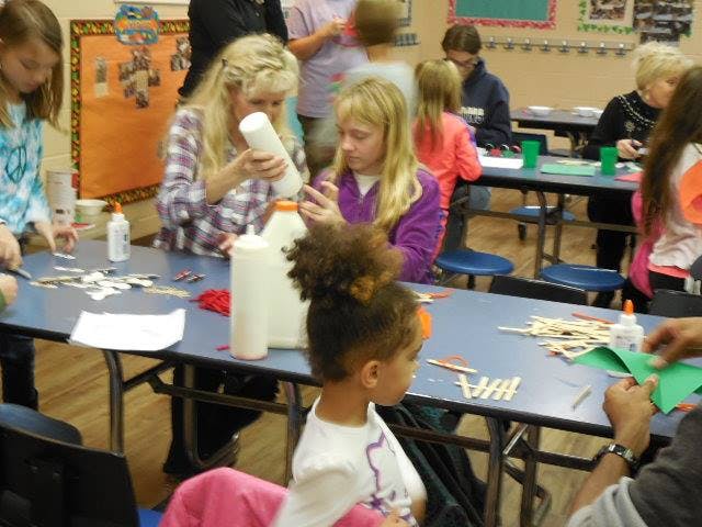 People and children at tables doing crafts with crafts with craft supplies