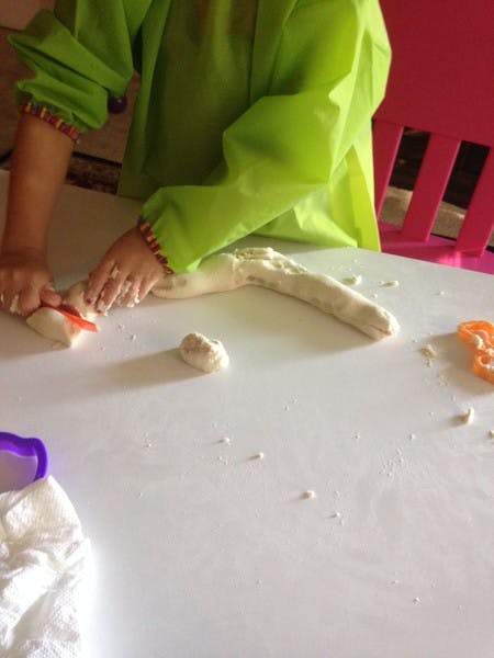 Person in green shirt cutting dough on a white table