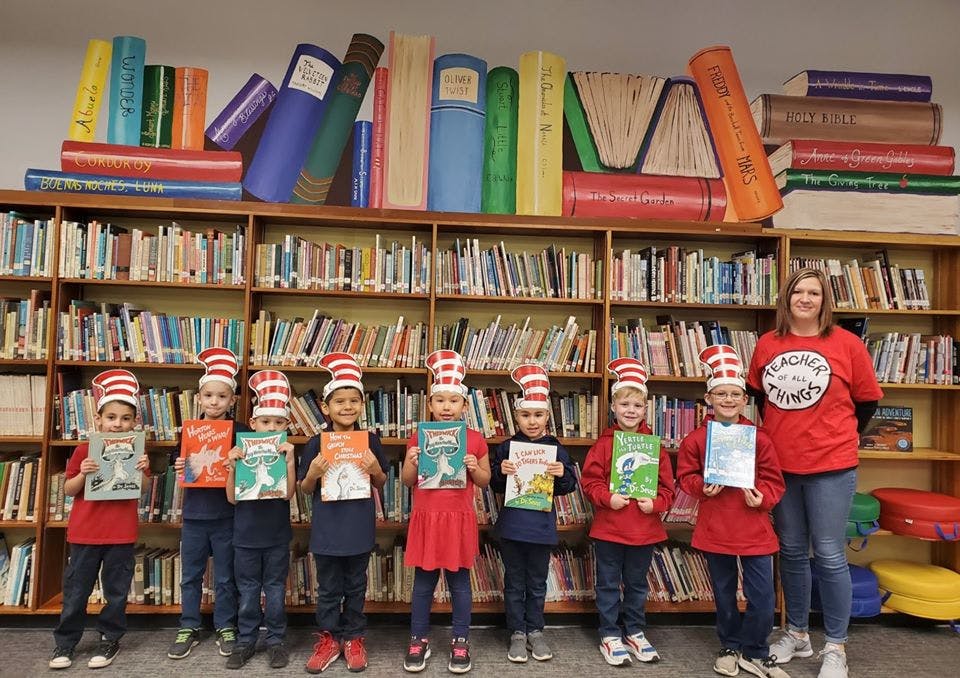 Adult and children in striped hats holding books in front of bookshelves