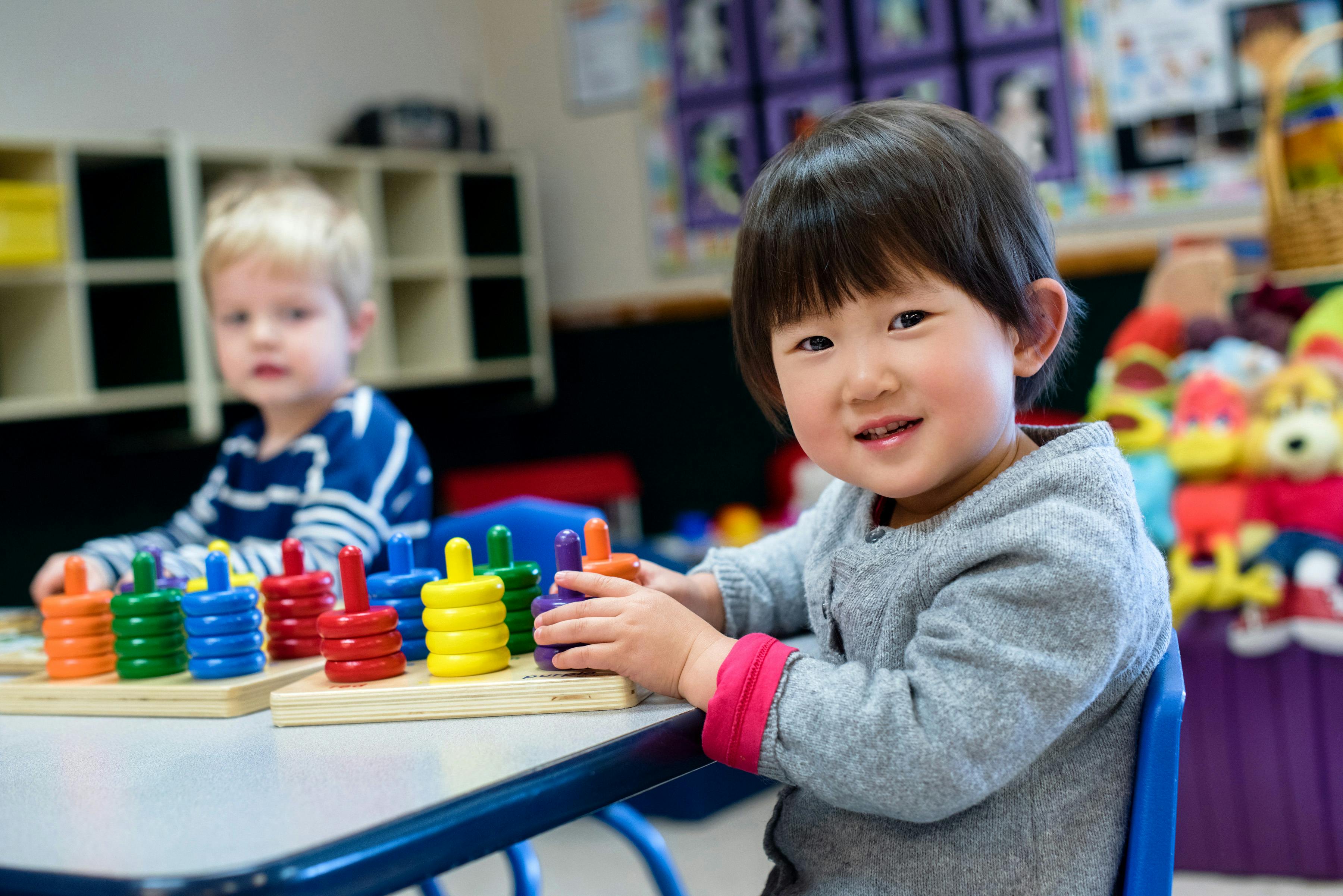 Two children playing with colorful stacking toys at a table in a classroom