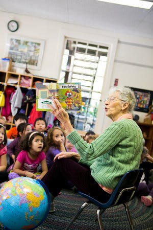 Person reading a book titled "Fire Safety" to a group of children in a classroom
