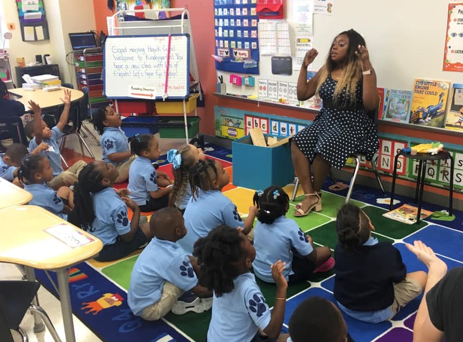 Person speaking to children sitting on the floor in a classroom