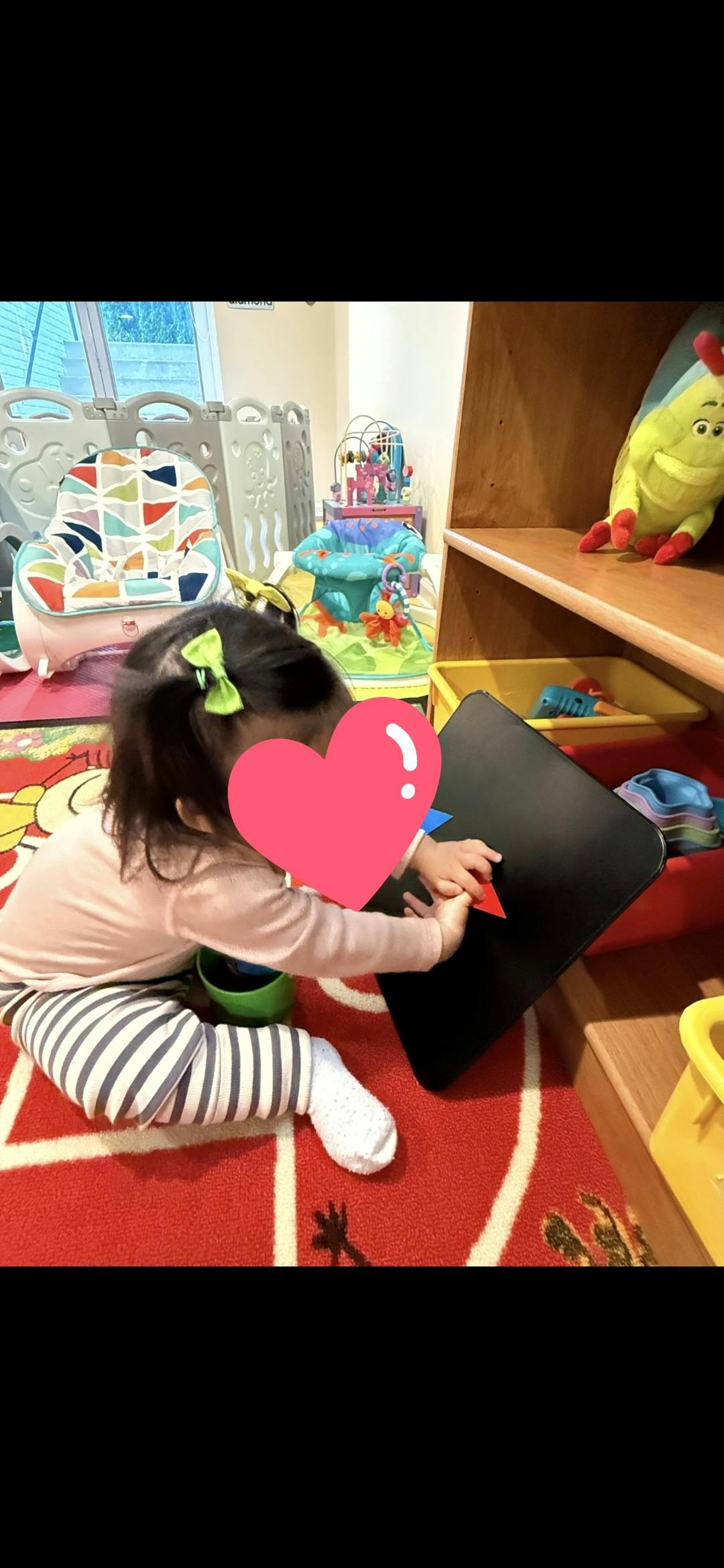 Child sitting on a play rug while handling a small board with colored shapes