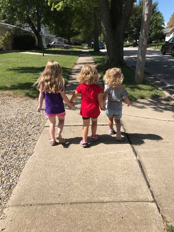Three children walking on a sidewalk holding hands