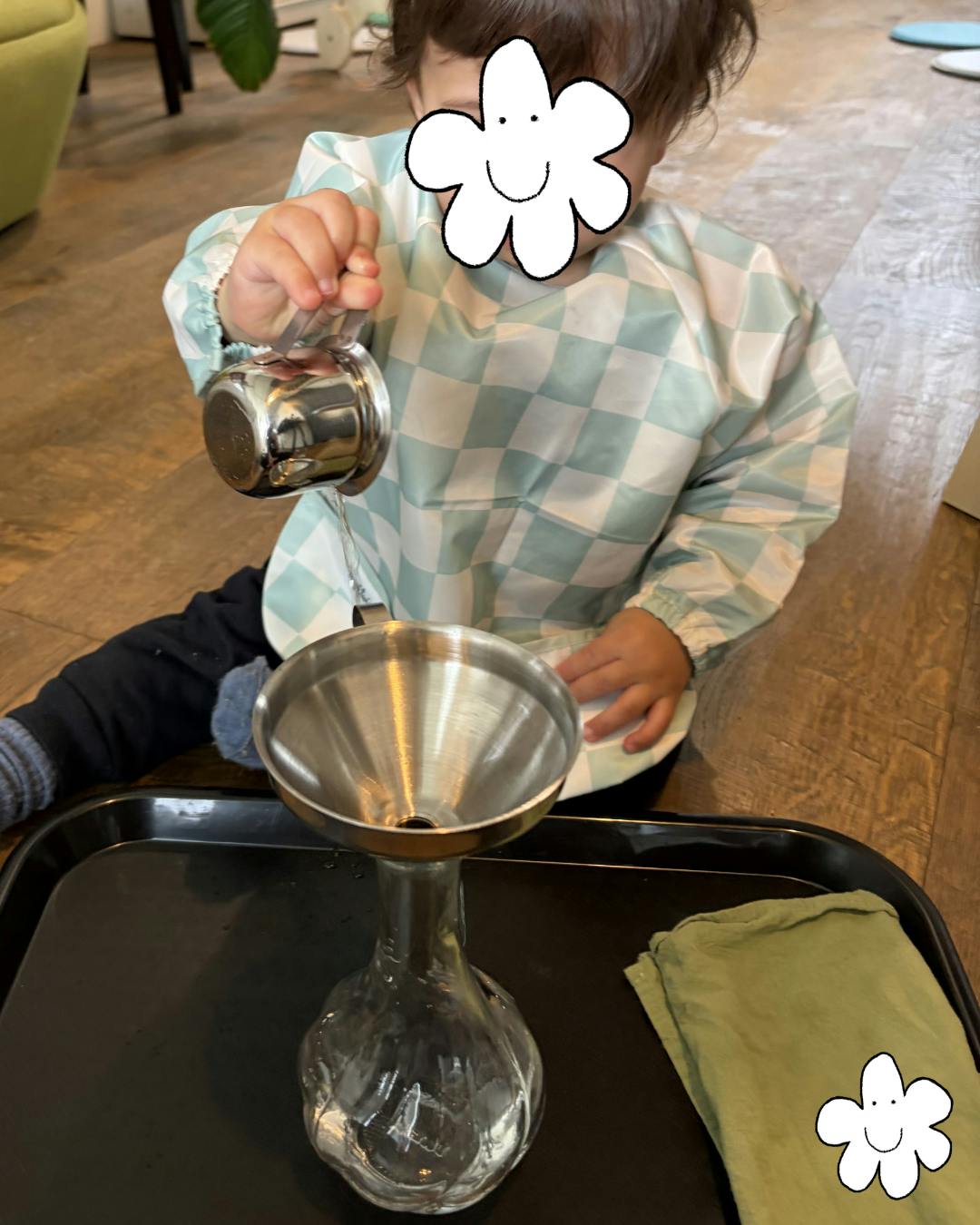Child in a checkered smock pouring water into a funnel