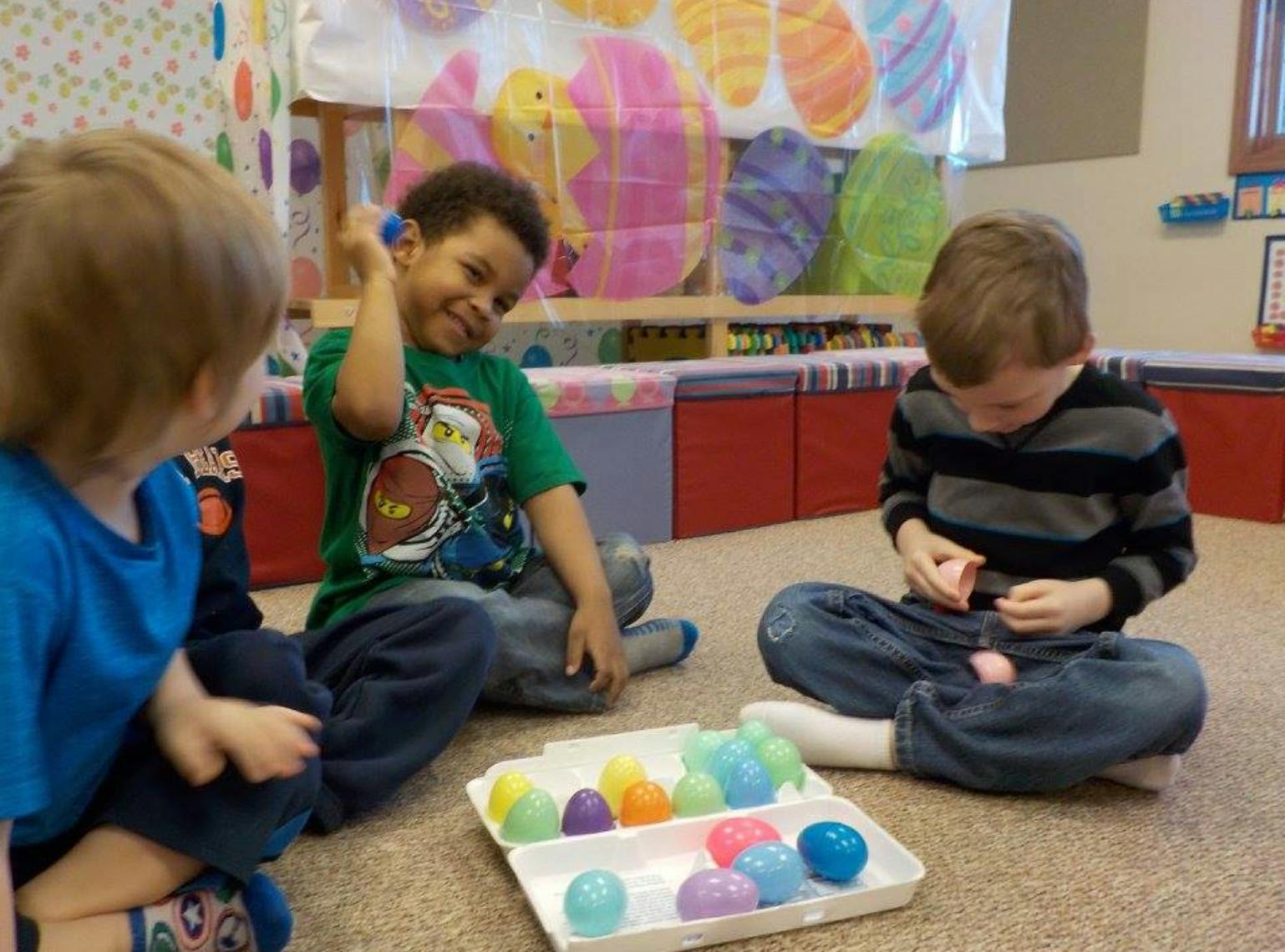 Three children sitting on the floor playing with colorful plastic eggs
