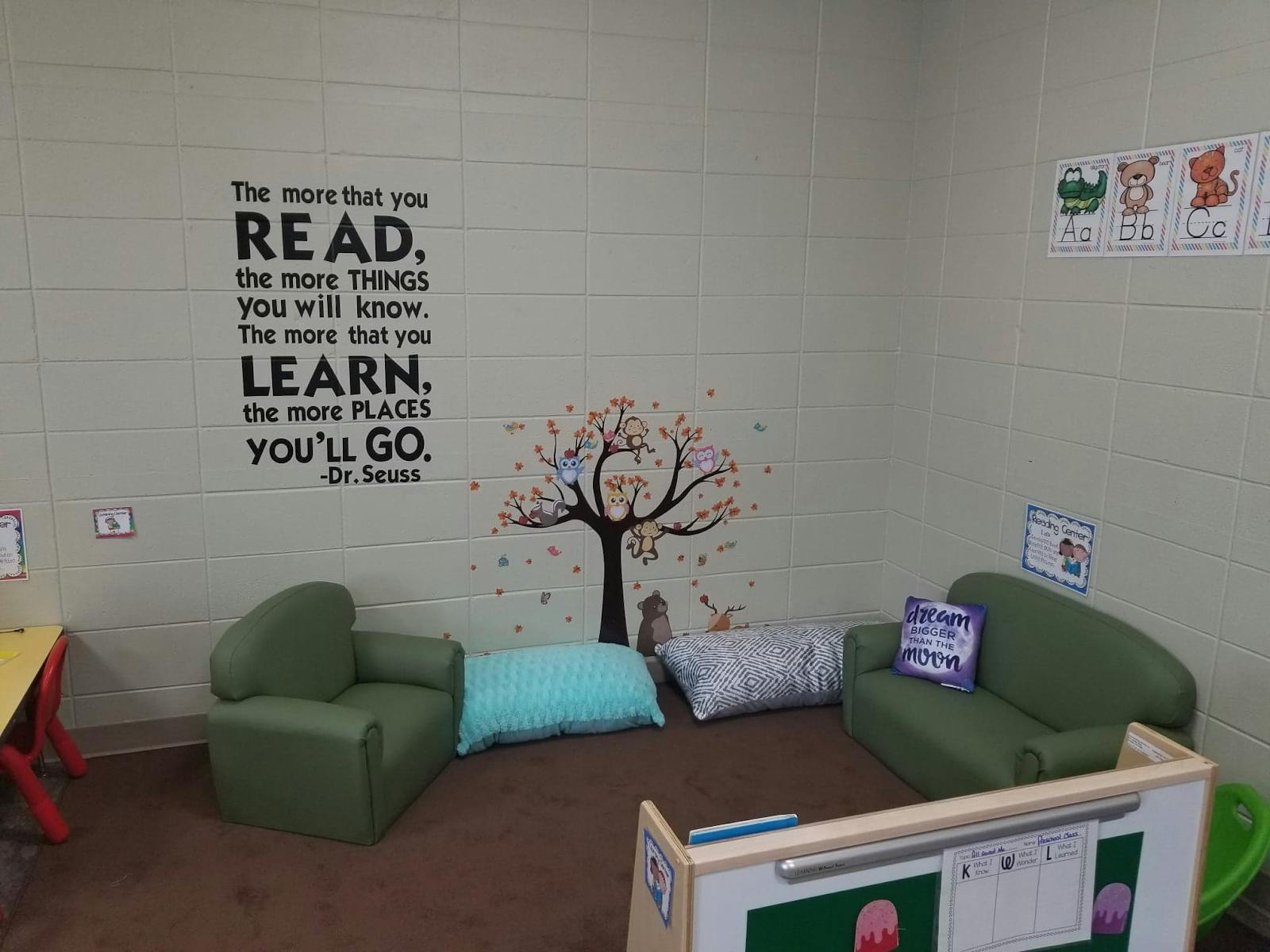 Reading nook with green chairs, pillows, and a wall decal with text