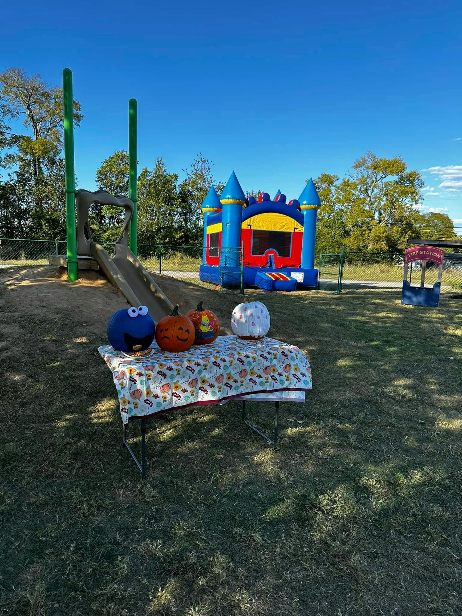 Decorative pumpkins on a table next to a playground slide and bounce house