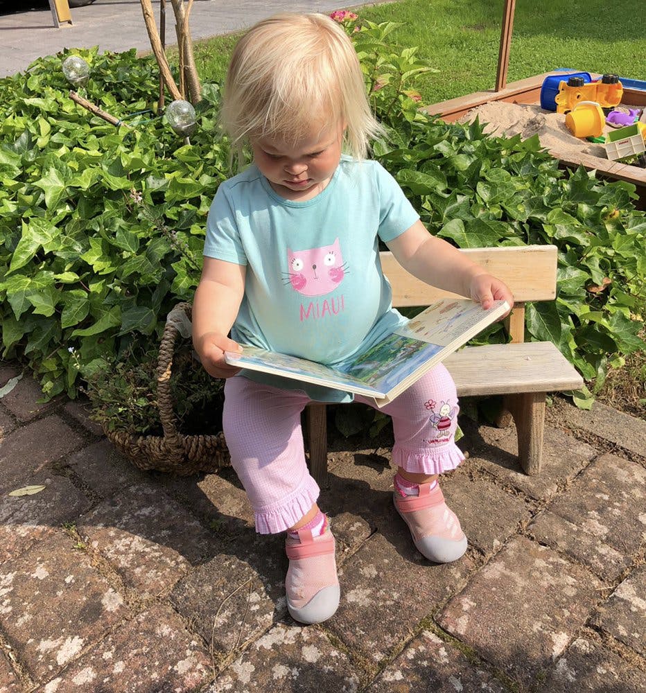 Child sitting on a bench reading a book outdoors