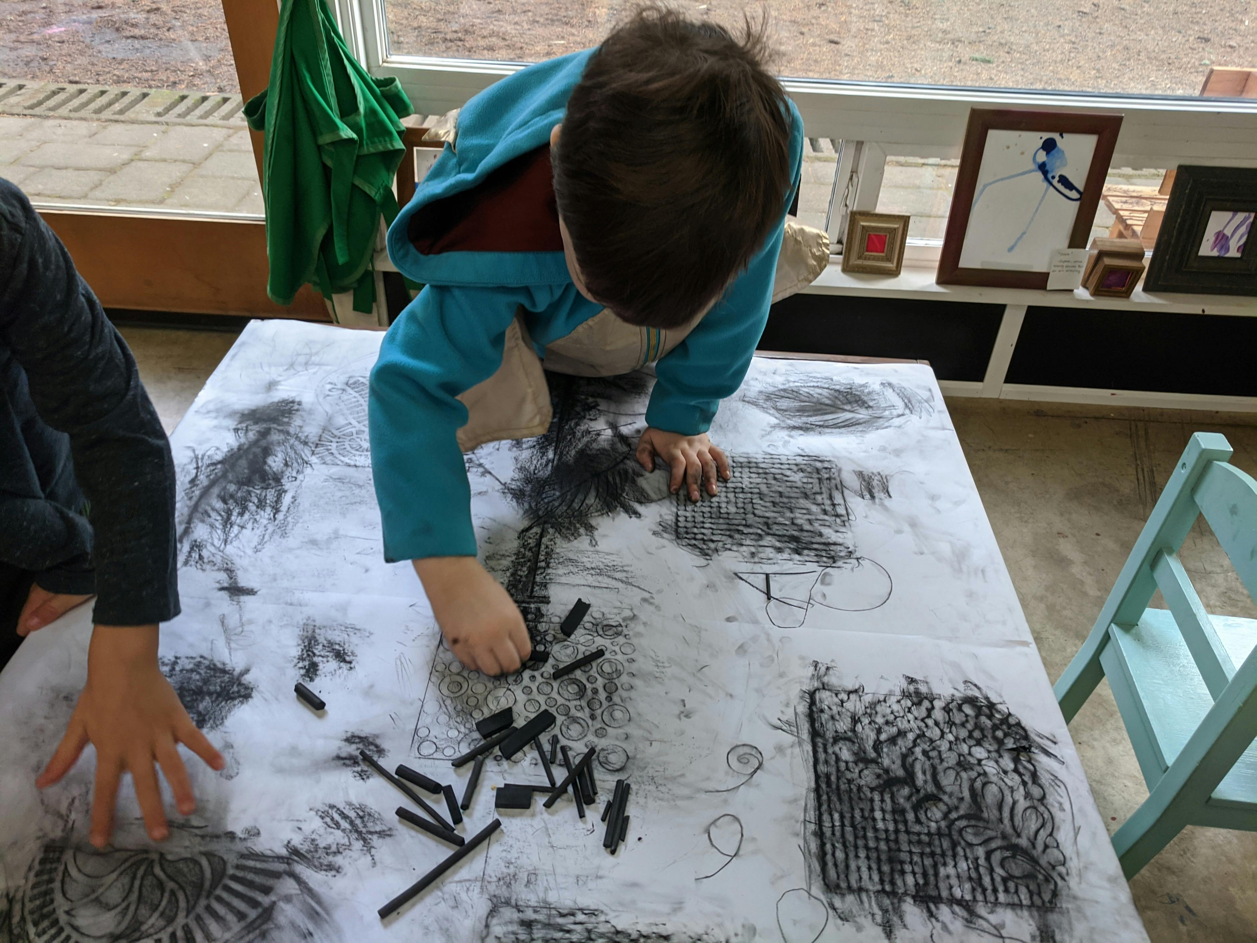 Child drawing on large paper with charcoal sticks