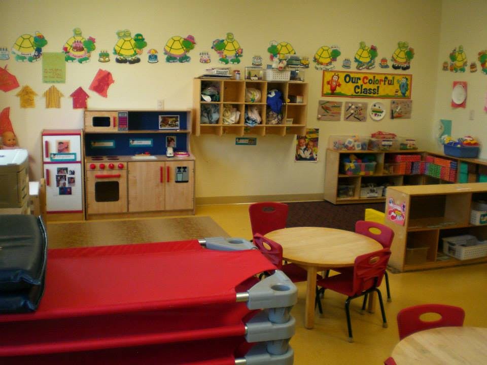 classroom with play kitchen, tables, and cots