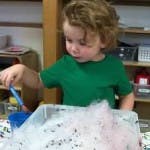 Child playing with bubbles in a container