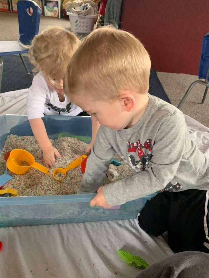 Two children playing in a sand table with toys