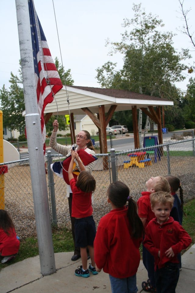 Person and child raising an American flag on a flagpole
