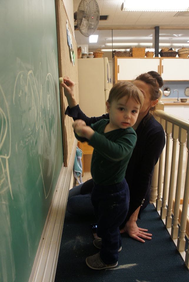 Child drawing on a chalkboard with a person kneeling nearby