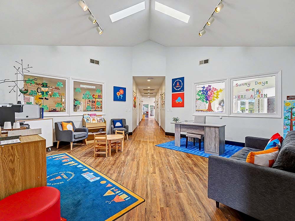 Lobby area with a wooden floor, blue rug, small chairs, couch, and windows