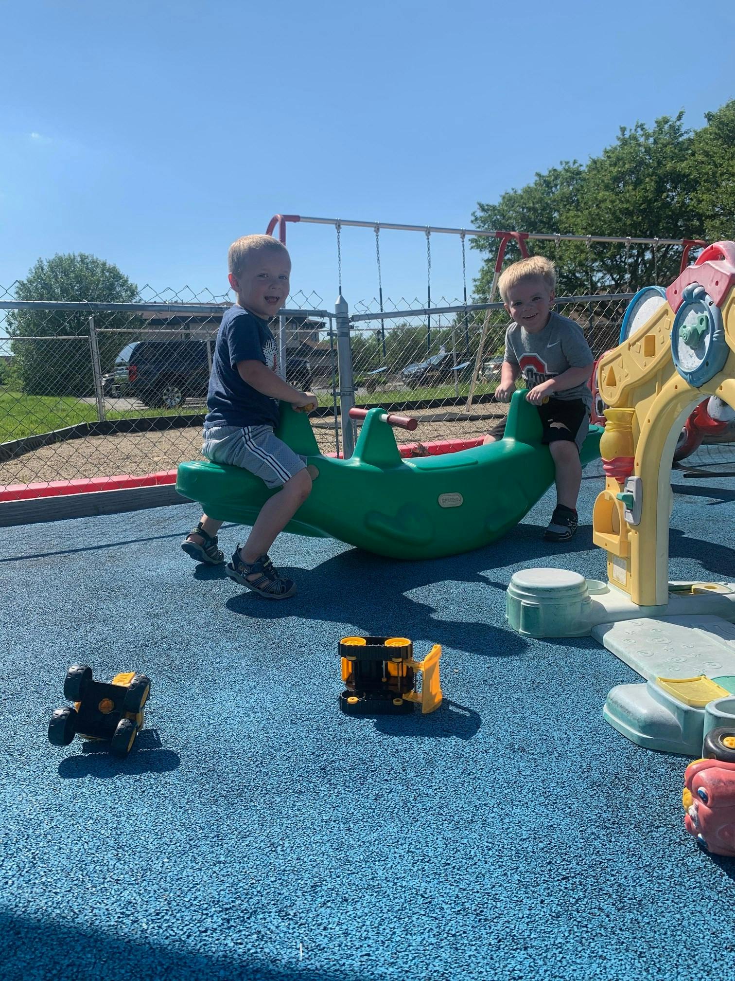 Two children playing on a green seesaw on a playground