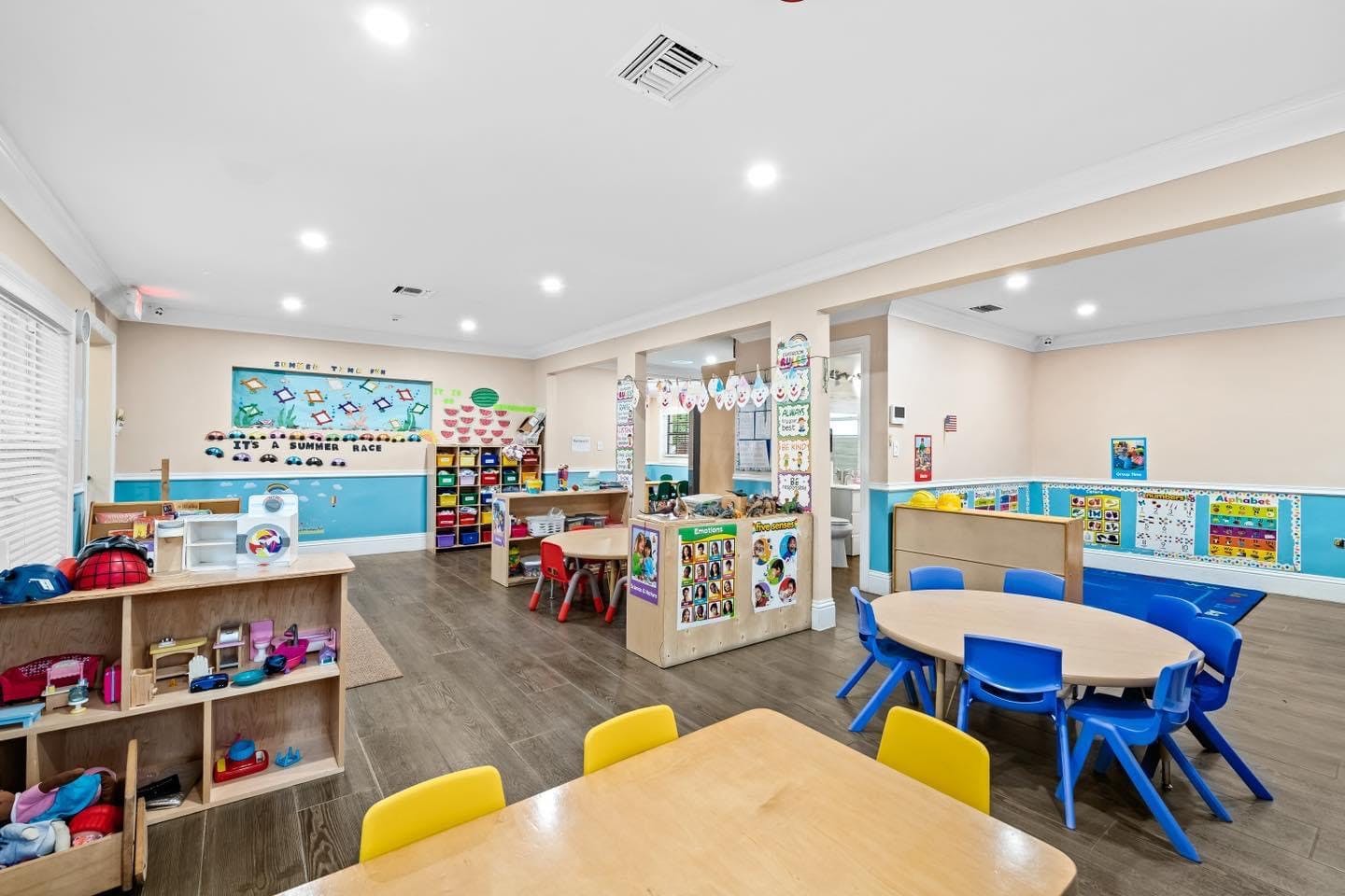 Classroom with small tables and chairs, shelves with toys and learning materials