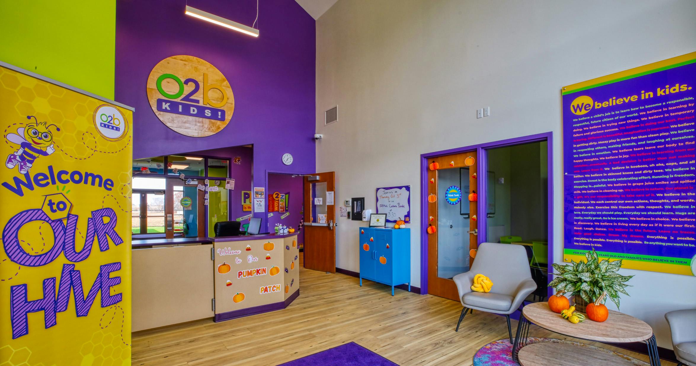 Reception area of a kids' facility with a "Welcome to Our Hive" banner and fall decorations