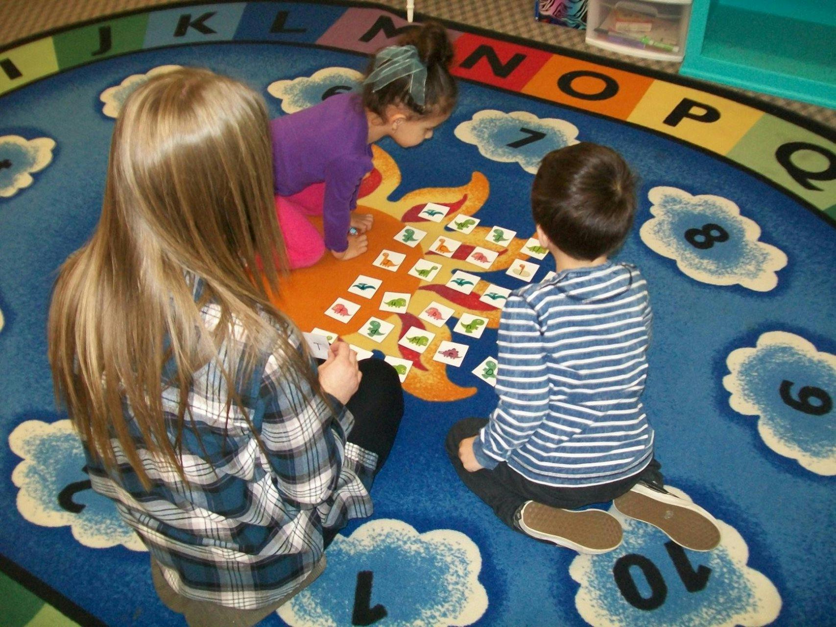 Three children playing a game on a colorful alphabet rug