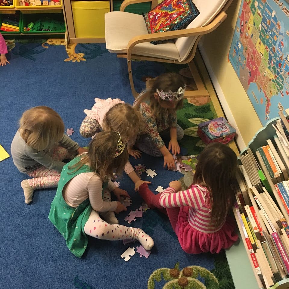 Children playing with puzzle pieces on a blue carpet in a classroom