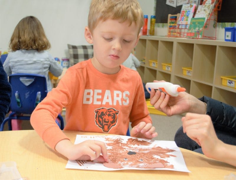 Child in orange shirt painting on paper at a table
